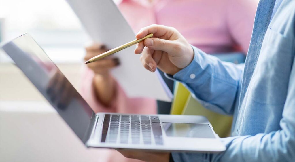 a man points at his laptop screen, mid-conversation—perhaps explaining how to upload a crucial document or navigate a VA portal. There's focus in his gesture and purpose in his expression.